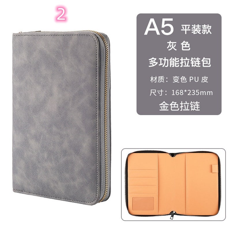 K&ouml;nnte beinhalten: Graues A5-Portfolio mit goldenem Rei&szlig;verschluss und strukturierter Oberfl&auml;che. Das Innere ist beige mit Kartenf&auml;chern und einer Tasche. Die Abmessungen betragen 16,8 cm x 23,5 cm.