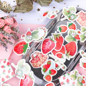 K&ouml;nnte beinhalten: Eine Bogen mit Aufklebern mit Aquarell-Illustrationen von Erdbeeren. Die Aufkleber befinden sich auf einem silbernen Tablett und zeigen Erdbeeren in K&ouml;rben, an Ranken und als einzelne Fr&uuml;chte. Die Aufkleber sind perfekt, um Tageb&uuml;chern, Planern und anderen Bastelprojekten einen Hauch von Verspieltheit zu verleihen.