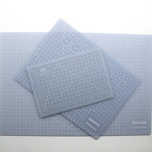 K&ouml;nnte beinhalten: Drei graue, selbstheilende Schneidematten mit Gitterlinien und Kreisen. Die Matten sind mit "Junesix Cutting Mats" beschriftet und haben unterschiedliche Gr&ouml;&szlig;en.