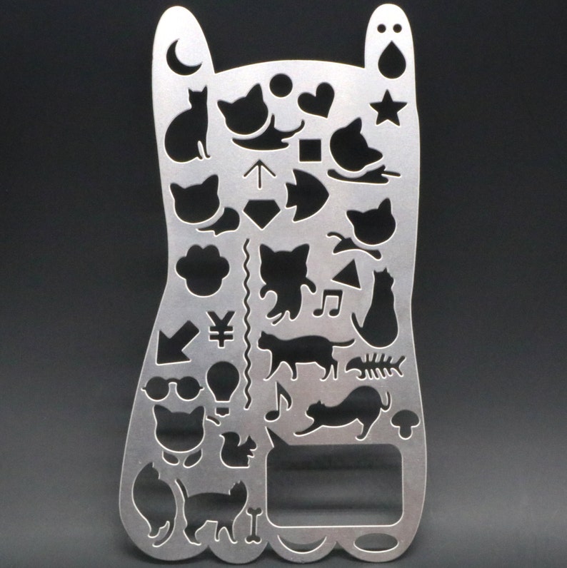 May include: A silver metal stencil with a cat theme. The stencil features various cat silhouettes, paw prints, hearts, stars, musical notes, and other designs.