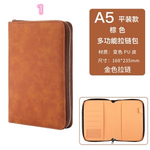 K&ouml;nnte beinhalten: Ein braunes A5-Portfolio mit Rei&szlig;verschluss. Das Portfolio ist aus PU-Leder gefertigt und hat einen goldfarbenen Rei&szlig;verschluss. Die Abmessungen betragen 16,8 cm x 23,5 cm. Der Innenraum hat mehrere Taschen und einen Kartenhalter.