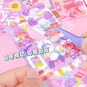 May include: A sheet of colourful stickers featuring cartoon characters, hearts, and other cute designs. The stickers are on a clear sheet with a glittery finish. The text "自帶裁切 即撕即貼" is printed on the sheet.