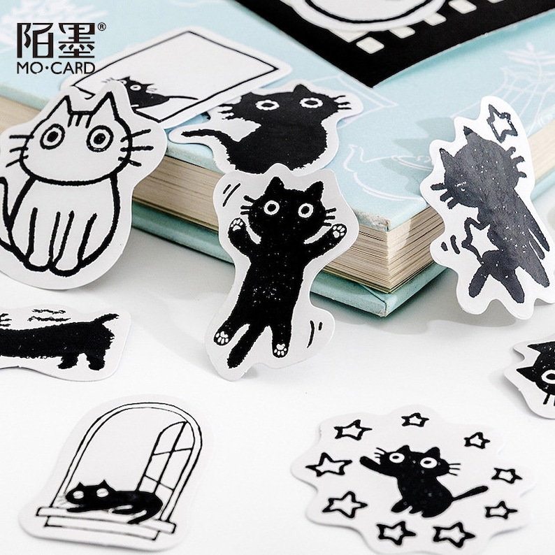 May include: A set of black and white cat stickers with various poses, including a cat sitting, a cat jumping, and a cat looking out a window. The stickers are on a white background and have a simple, minimalist design.
