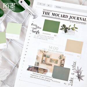 May include: A green and white journal with a grid pattern and stickers. The stickers feature a green color swatch with the text "PANTONE 22", a photo of a room with a speaker and plants, and a brown color swatch with the text "PANTONE 45". The journal also has the text "The Mocard Journal" and "The 100 Life Magazines 001/Plant".