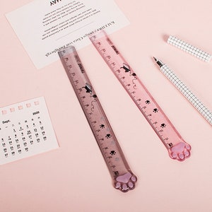 May include: Two pink plastic rulers with paw print designs and black cat illustrations. The rulers are 30.5 cm long and have a paw print shaped end.