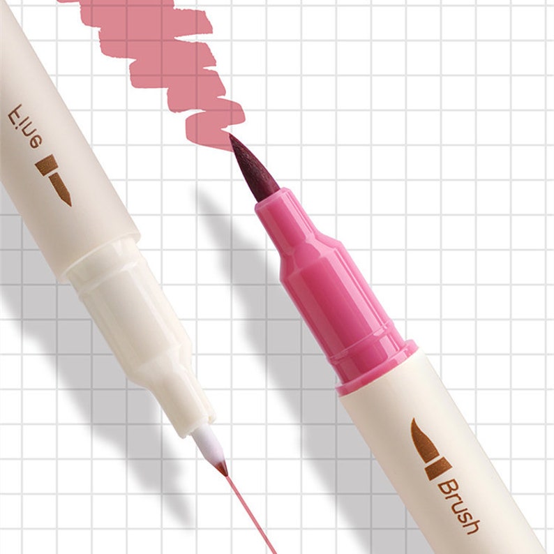 May include: Close-up of two dual-tip markers, one with a fine tip and the other with a brush tip. The brush tip marker is magenta, and the fine tip marker is white. A swatch of pink ink is visible, along with a pink line drawn by the fine tip marker.