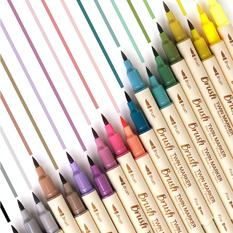 May include: A collection of colorful twin markers with black tips, arranged diagonally on a white surface with pastel-colored stripes. The markers are labeled "Brush TWIN MARKER" and "Fine". The markers are in various colors, including brown, purple, pink, orange, blue, green, and yellow.
