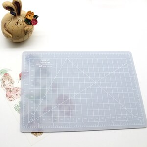 K&ouml;nnte beinhalten: Eine graue, selbstheilende Schneidematte mit einem Rastermuster und wei&szlig;en Linien. Die Matte ist mit "Junesix Cutting Mats HIGHLY DURABLE QUALITY A5 Size: 30x45cm" beschriftet.