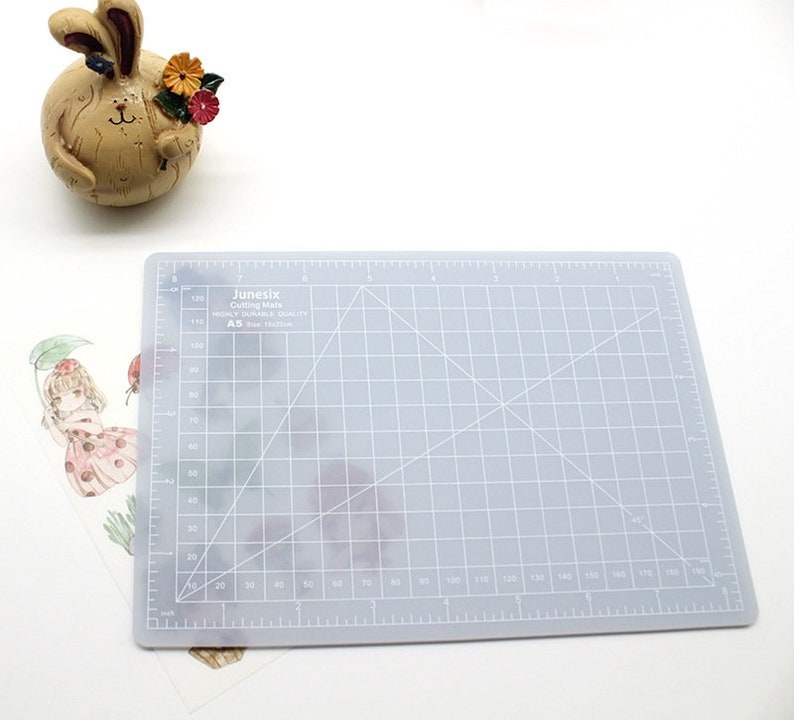 K&ouml;nnte beinhalten: Eine graue, selbstheilende Schneidematte mit einem Rastermuster und wei&szlig;en Linien. Die Matte ist mit "Junesix Cutting Mats HIGHLY DURABLE QUALITY A5 Size: 30x45cm" beschriftet.