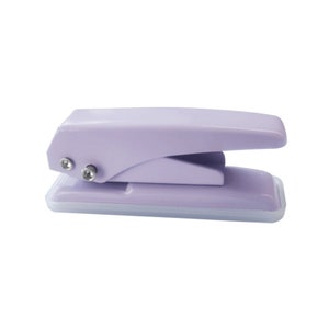 May include: A lavender-colored handheld paper punch with a white base. The punch has a lever on top and two silver screws on the side.