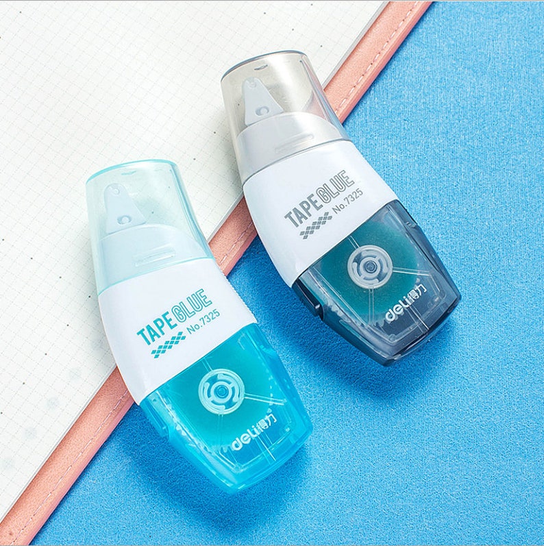 May include: Two blue and white tape glue dispensers with the text "TAPE GLUE" and "No. 7325" on the front. The dispensers are on a blue surface.