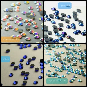 May include: Assortment of rhinestones in various colours, including crystals AB, jet AB, blue, and aquamarine AB. The rhinestones are arranged in groups on a white background.