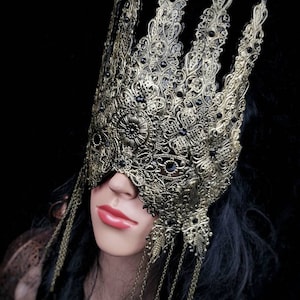 Puede incluir: Una m&aacute;scara de masquerade de oro en forma de corona con detalles negros y cadenas colgantes. La m&aacute;scara est&aacute; hecha de metal y tiene un dise&ntilde;o delicado e intrincado.