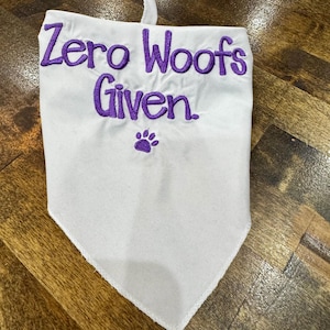 May include: White dog bandana with purple embroidery that reads "Zero Woofs Given" with a paw print below the text.
