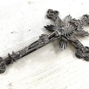 May include: An ornate silver crucifix depicting Jesus Christ. The cross has decorative scrollwork at the ends and a sunburst design behind Christ's head. A detailed religious item.