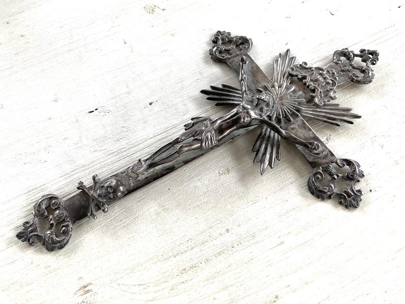 May include: An ornate silver crucifix depicting Jesus Christ. The cross has decorative scrollwork at the ends and a sunburst design behind Christ's head. A detailed religious item.