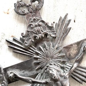 May include: An antique silver-coloured crucifix with intricate detailing. The cross depicts Jesus Christ, with the inscription "INRI" above. The design includes ornate embellishments and sunburst rays emanating from behind the figure.