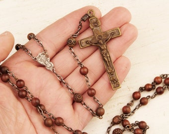 May include: A vintage rosary with brown wooden beads and a bronze crucifix. The crucifix features a detailed depiction of Jesus Christ. The rosary chain is made of metal. The beads are connected by a metal chain.