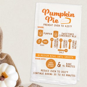 May include: A white kitchen towel with an orange pumpkin pie recipe. The recipe includes ingredients like pumpkin, condensed milk, cinnamon, ginger, nutmeg, and salt. It also includes instructions for baking the pie at 425 degrees Fahrenheit for 15 minutes, then reducing the oven temperature to 350 degrees Fahrenheit and baking for 35 to 40 minutes.