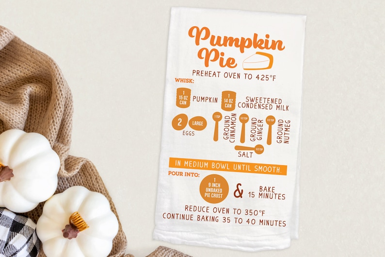 May include: A white kitchen towel with an orange pumpkin pie recipe. The recipe includes ingredients like pumpkin, condensed milk, cinnamon, ginger, nutmeg, and salt. It also includes instructions for baking the pie at 425 degrees Fahrenheit for 15 minutes, then reducing the oven temperature to 350 degrees Fahrenheit and baking for 35 to 40 minutes.