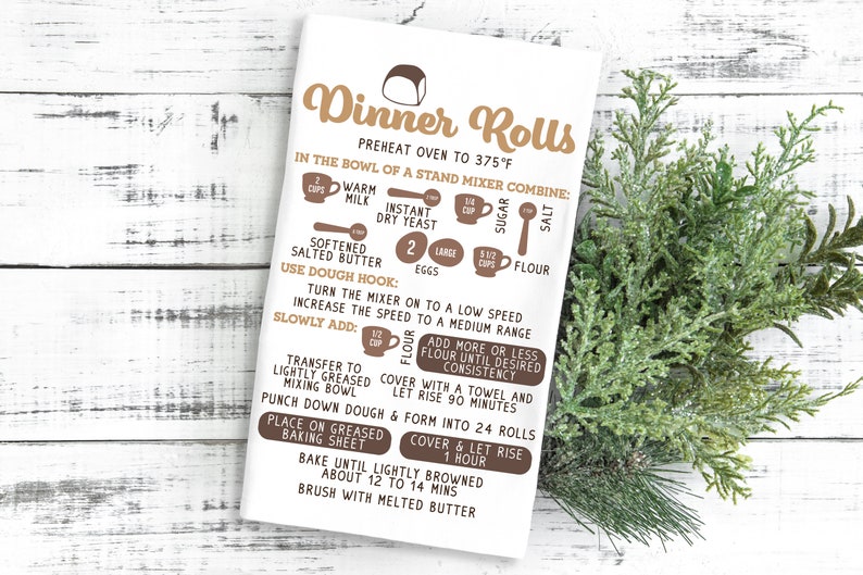 May include: A white kitchen towel with brown text and illustrations showing the ingredients and steps for making dinner rolls. The text includes "Dinner Rolls", "Preheat oven to 375&deg;F", "In the bowl of a stand mixer combine:", "Warm milk", "Instant dry yeast", "Softened salted butter", "2 large eggs", "5 1/2 cups flour", "Sugar", "Salt", "Use dough hook:", "Turn the mixer on to a low speed", "Increase the speed to a medium range", "Slowly add:", "Flour", "Transfer to lightly greased mixing bowl", "Add more or less flour until desired consistency", "Cover with a towel and let rise 90 minutes", "Punch down dough & form into 24 rolls", "Place on greased baking sheet", "Cover & let rise 1 hour", "Bake until lightly browned about 12 to 14 mins", "Brush with melted butter".