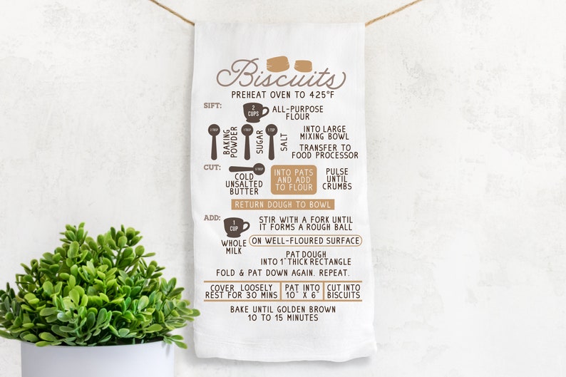 May include: A white kitchen towel with brown text and illustrations showing the steps for making biscuits. The text includes "Biscuits", "Preheat oven to 425&deg;F", "Sift", "Cut", "Add", "Fold & Pat", "Cover Loosely", "Rest for 30 mins", "Pat into", "Cut into", "Bake until golden brown 10 to 15 minutes".