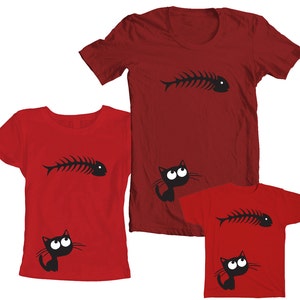 May include: Three red t-shirts with a black cat and fishbone design. The largest shirt has a fishbone on the front and a cat looking up at it. The medium shirt has a cat looking up at a fishbone on the front. The smallest shirt has a cat looking up at a fishbone on the front.