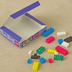 Puede incluir: Una caja abierta de bloques de construcción LEGO Friends. La caja es morada y blanca con el logotipo de LEGO Friends. La caja contiene una variedad de ladrillos LEGO de colores, incluidos azul, rojo, verde, amarillo, blanco y negro.