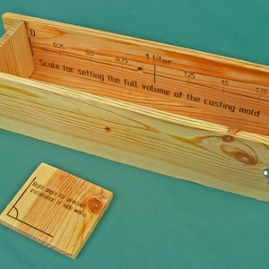 Può includere: Stampo in legno per colata con scala per la misurazione del volume, fino a 1 litro. Include un piccolo quadrato di legno con testo sugli angoli retti. Lo stampo è in legno chiaro e ha ferramenta metallica.