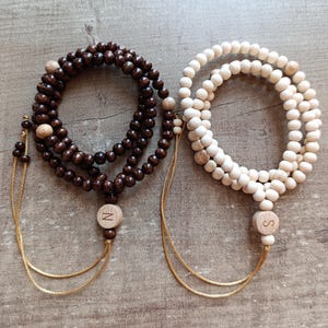 May include: Two wooden beaded necklaces with brown and white beads. The necklaces have a tassel at the end with a letter charm, one says "N" and the other says "S".