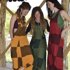 Może przedstawiać: Trzy osoby w kombinezonach z patchworku w różnych kolorach i wzorach. Kombinezony są wykonane z różnych tkanin i mają kratkowany wzór. Osoby stoją w drewnianej konstrukcji.