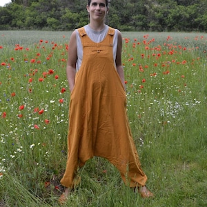 Puede incluir: Una mujer lleva un mono amarillo mostaza con un solo cierre de botón en el escote. Está de pie en un campo de flores silvestres, incluyendo amapolas rojas.
