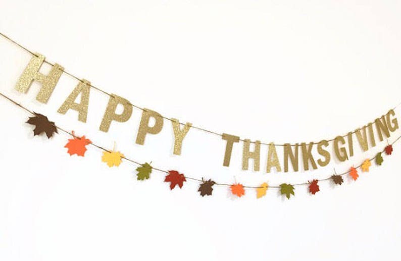 Może przedstawiać: Złota girlanda z błyszczącymi literami z napisem "Happy Thanksgiving" przewleczona przez brązowy sznurek i ozdobiona papierowymi liśćmi w jesiennych kolorach.