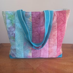 May include: A turquoise and purple striped tote bag with a turquoise fabric handle. The bag is made of a patchwork of different fabrics with a speckled pattern.