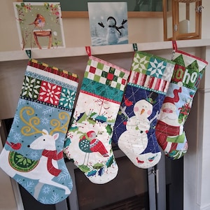 May include: Four festive Christmas stockings with various designs, including a reindeer, birds, a snowman, and Santa Claus. Each stocking features unique patterns and colours, with red, green, and blue accents. The stockings are suspended from a mantelpiece.