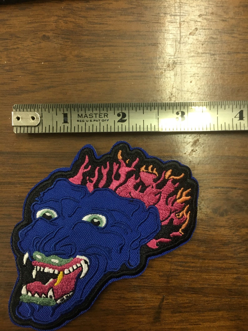 Pu&ograve; includere: Toppa ricamata con un volto di mostro blu con occhi verdi, una bocca spalancata e fiamme rosa. La toppa misura circa 7,6 cm di larghezza.