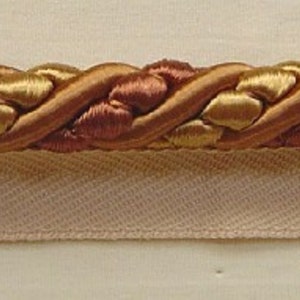 May include: A close-up of a braided trim with a gold and copper color scheme. The trim is woven with a rope-like texture.