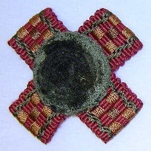 May include: A dark green velvet button with a red and gold braided trim. The trim has a checkered pattern.