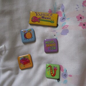 May include: Five colorful magnets with different music-themed designs. The magnets feature a guitar, a drum set, a record player, a saxophone, and the text "Music Yahoo! .com".