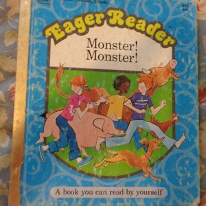 May include: A blue and yellow book cover with the title "Eager Reader" and the words "Monster! Monster!" in white text. The cover features an illustration of children playing with a pig, a dog, and a cow. The book is part of the "A Little Golden Book" series.