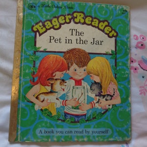 May include: A vintage Golden Book titled "The Pet in the Jar" from the Eager Reader series. The cover features three children, two girls and a boy, looking at a jar with a stick inside. The book is green and blue with a gold spine.