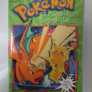 May include: A book cover featuring the Pokemon characters Pikachu and Charizard. The book title is "Pokemon Thundershock in Pummelo Stadium". The book is published by Scholastic and adapted by Tracey West. The book cover has a green background with a yellow and red Pokemon logo.
