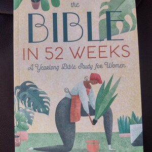 May include: Book cover with an illustration of a person gardening. The title is "The Bible in 52 Weeks: A Yearlong Bible Study for Women" by Dr. Kimberly D. Moore.