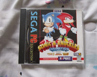 May include: A Sega PC Collection CD case featuring Sonic & Knuckles. The case is black with a red, blue, and yellow design. The text on the case reads "SEGA PC COLLECTION", "SONIC & KNUCKLES COLLECTION", "FEATURING: SONIC 3, SONIC & KNUCKLES, SONIC", "Y2K", "Distributed Exclusively by: EXPERT SOFTWARE", and "KA".