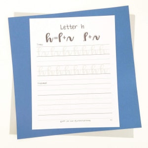 May include: A white paper with calligraphy practice for the letter "h" is displayed on a blue background. The paper includes the letter "h" broken down into strokes, with tracing and freehand sections. The text "Letter h" is at the top.