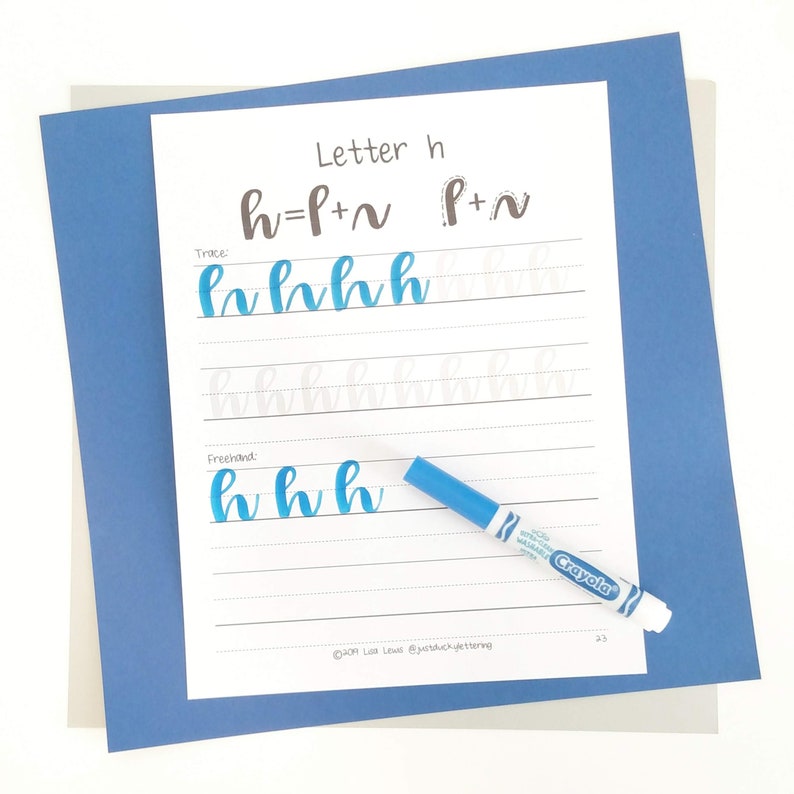 May include: A calligraphy practice sheet for the letter "h" with instructions and examples. The sheet includes the text "Letter h", "h=P+~ P+~", and "Trace:" and "Freehand:". A blue Crayola marker is on the sheet. The sheet is on a blue and gray background.