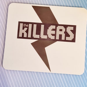 May include: White mousepad with a brown lightning bolt graphic. The word "the KILLERS" is in white letters with a dotted pattern inside the letters.