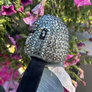 May include: A silver-colored, bedazzled Mickey Mouse ear headband. The ears are covered in small, sparkling rhinestones. The headband has a black velvet band and a tag that reads "DisneyStore.com".