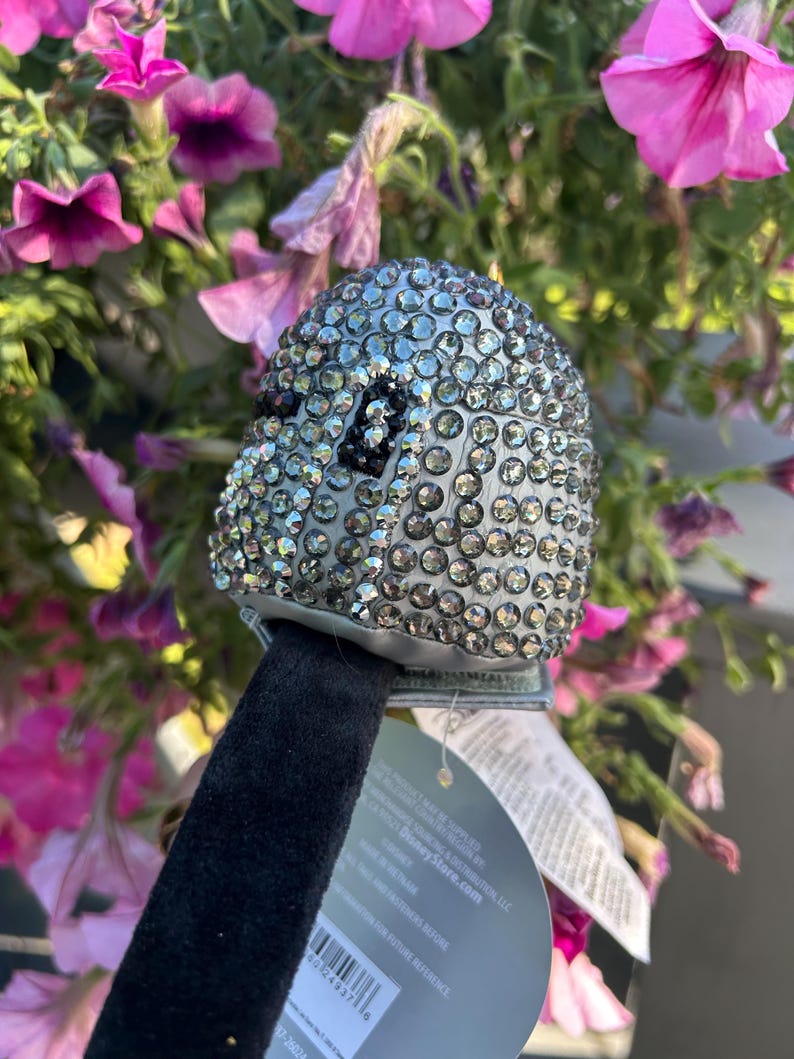 May include: A silver-colored, bedazzled Mickey Mouse ear headband. The ears are covered in small, sparkling rhinestones. The headband has a black velvet band and a tag that reads "DisneyStore.com".
