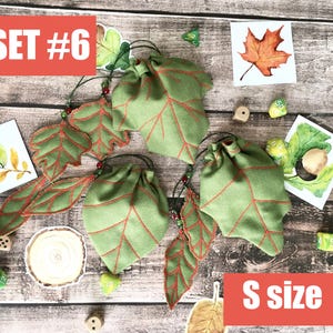 May include: Green leaf-shaped drawstring bags with red vein detailing, labeled "S size" and "SET #6". The bags are accompanied by leaf-shaped embellishments and watercolor illustrations of leaves. Dice are scattered around the bags.
